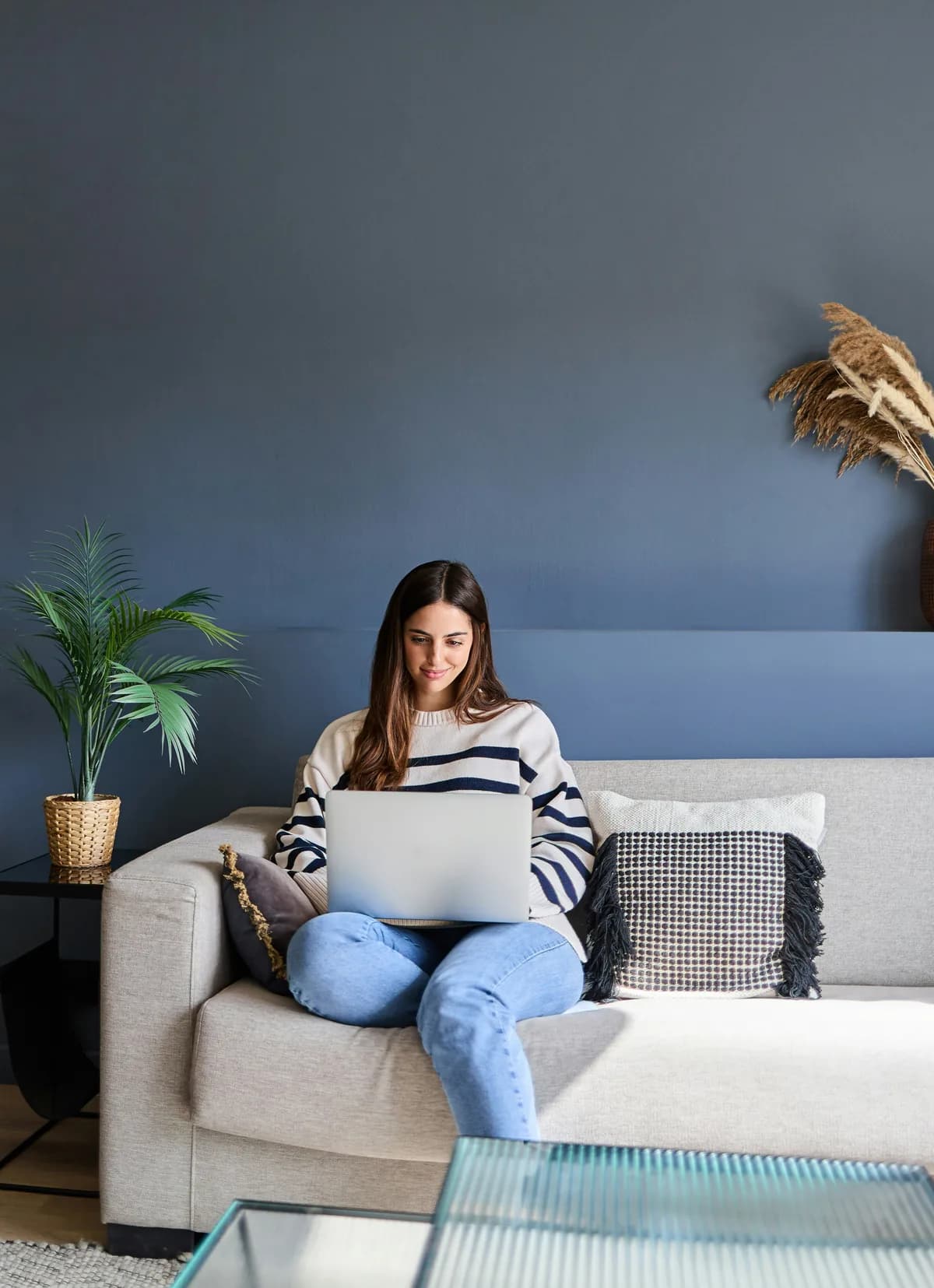 A woman in a striped sweater sitting on a couch using a laptop in a calm living room